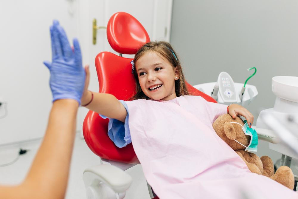 a girl holding her teddy bear while sitting in a dental chair